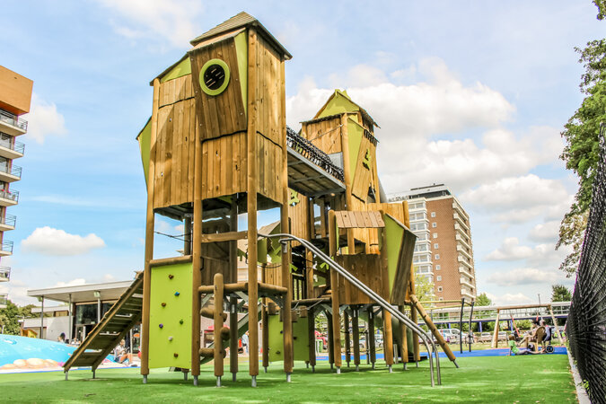 Öffentliche Spielanlagen – eibe Spielanlage auf einer Grünfläche inmitten einer Stadtkulisse. 