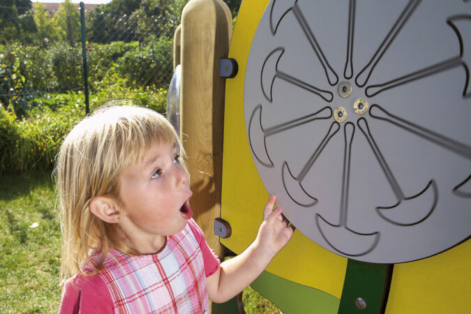 Kindergarten-Spielgeräte von eibe – kleines Mädchen dreht an einem Spielrad der gelben eibe Spielanlage.