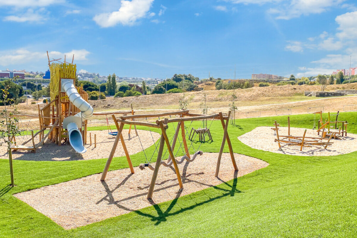 Öffentliche Spielanlagen – eibe Spielanlage auf einer gepflegten Grünfläche vor einer städtischen Kulisse. 