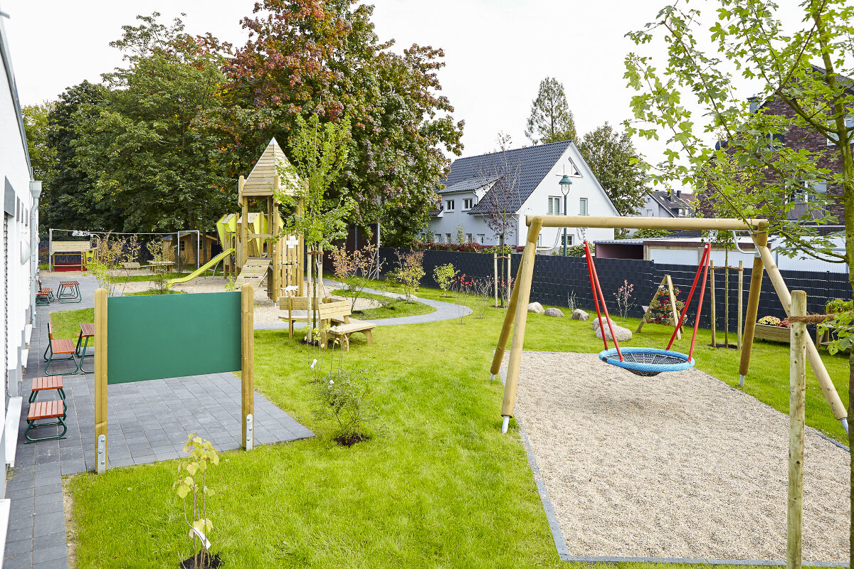 Kindergarten-Spielgeräte von eibe – Spielanlage mit Spielturm, Nestschaukel über sandiger Fläche und diversen Sitzgelegenheiten.